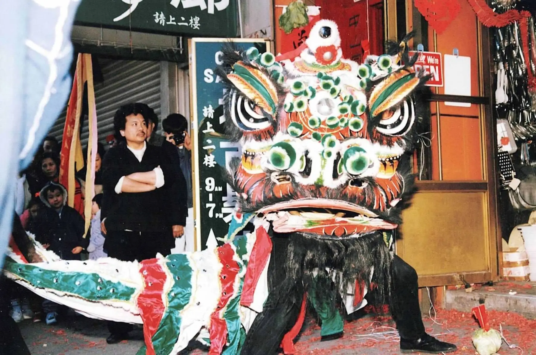 A green, white, and red lion head with Sifu Tony Lau standing behind it